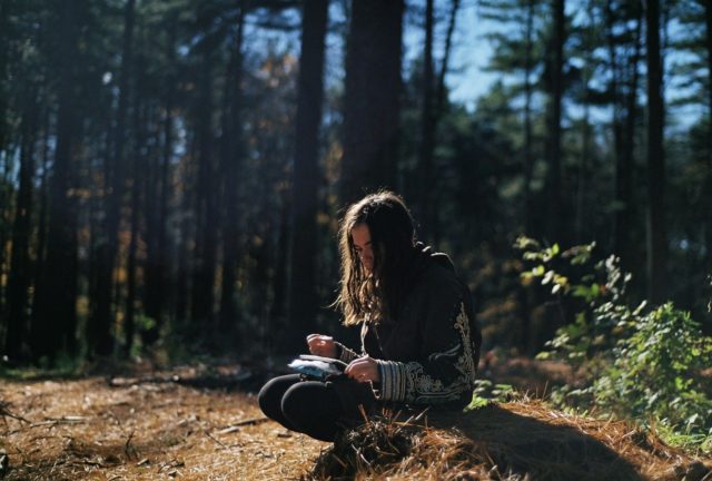 woman writing in journal in the woods