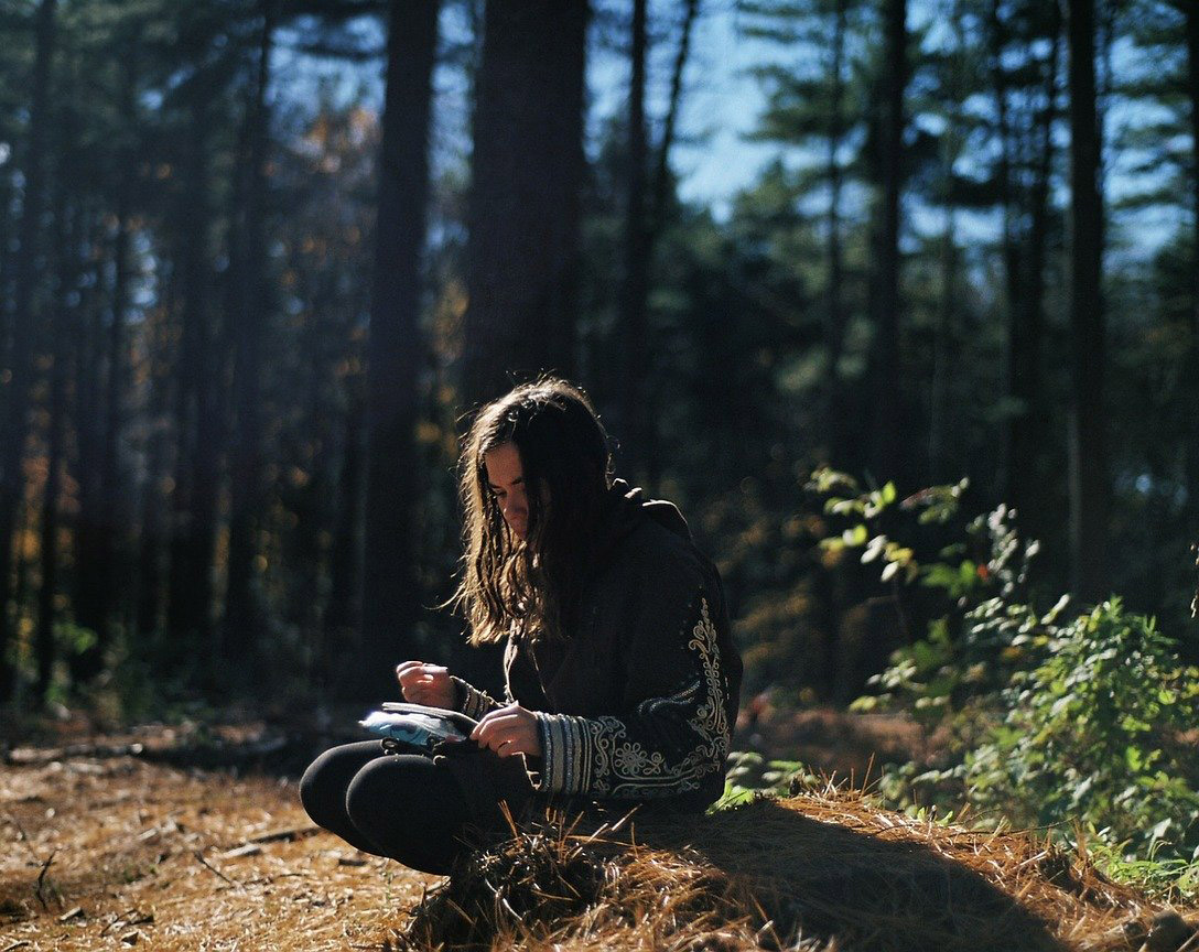 woman sitting in forest writing in notebook